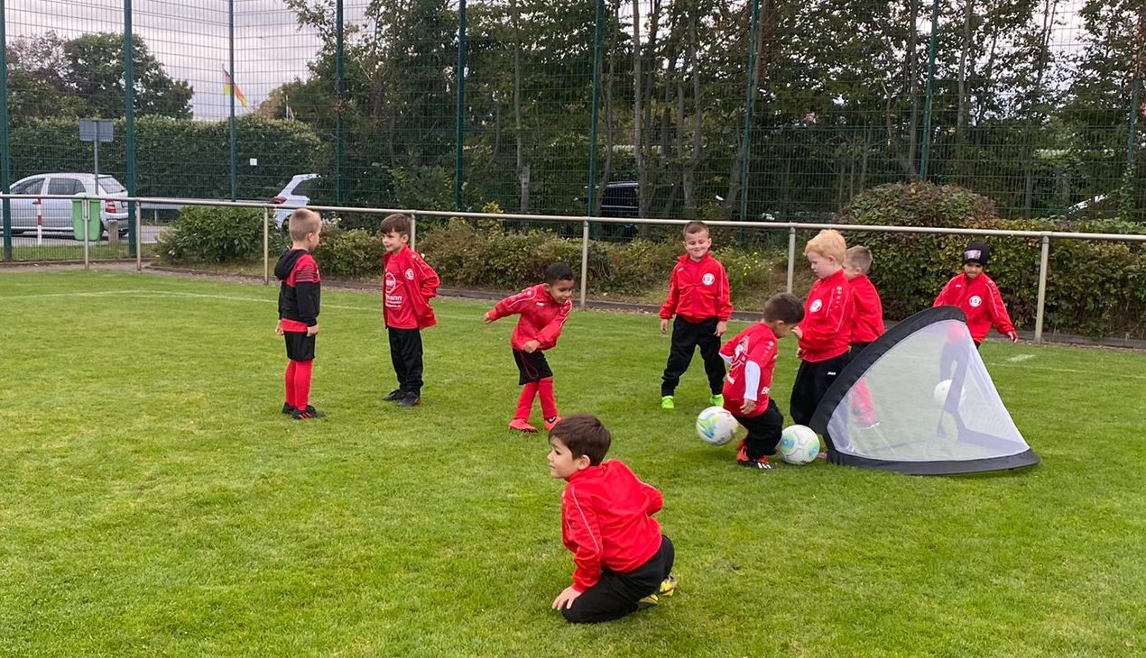 Kinder in roten SV-07-Trainingsanzügen beim Funino-Training am Mini-Tor auf dem Rasenplatz