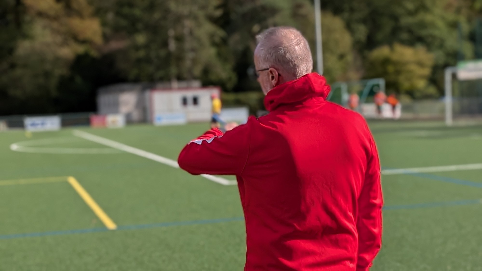 Betreuer des SV 07 Raunheim im roten Trainingsanzug von hinten an der Seitenlinie im Sportpark