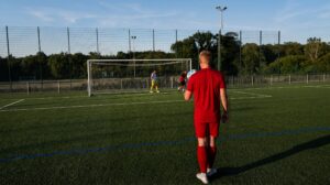 Spieler des SV 07 Raunheim im roten Trikot von hinten mit dem Ball in der Hand, im Hintergrund Tor und Torwart