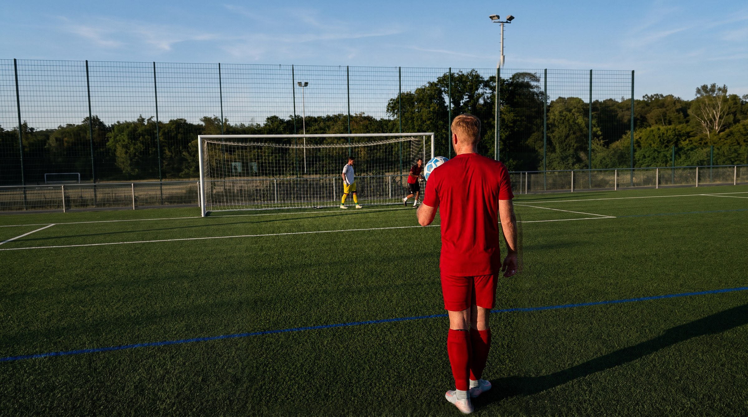 Spieler des SV 07 Raunheim im roten Trikot von hinten mit dem Ball in der Hand, im Hintergrund Tor und Torwart