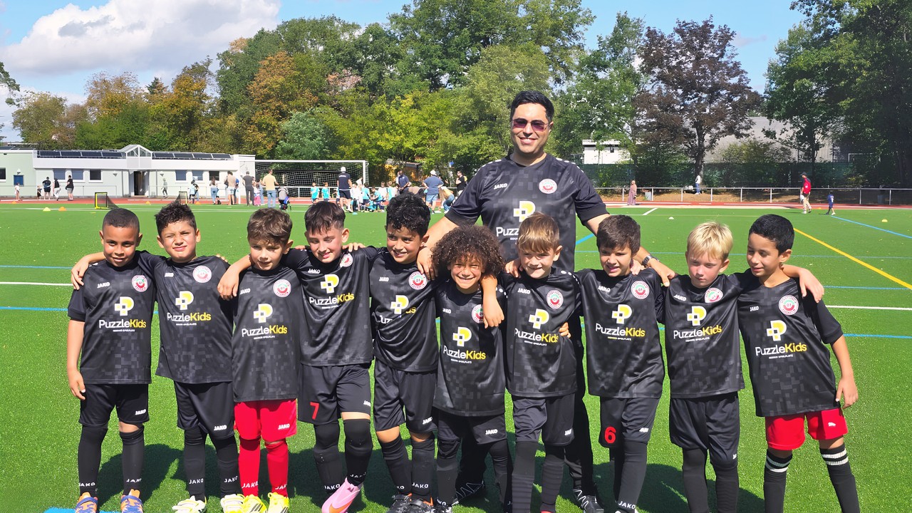 Mohamed Bellafkir steht hinter Kindern der F-Jugend des SV 07 Raunheim in schwarzen Trikots auf einem Kunstrasenplatz